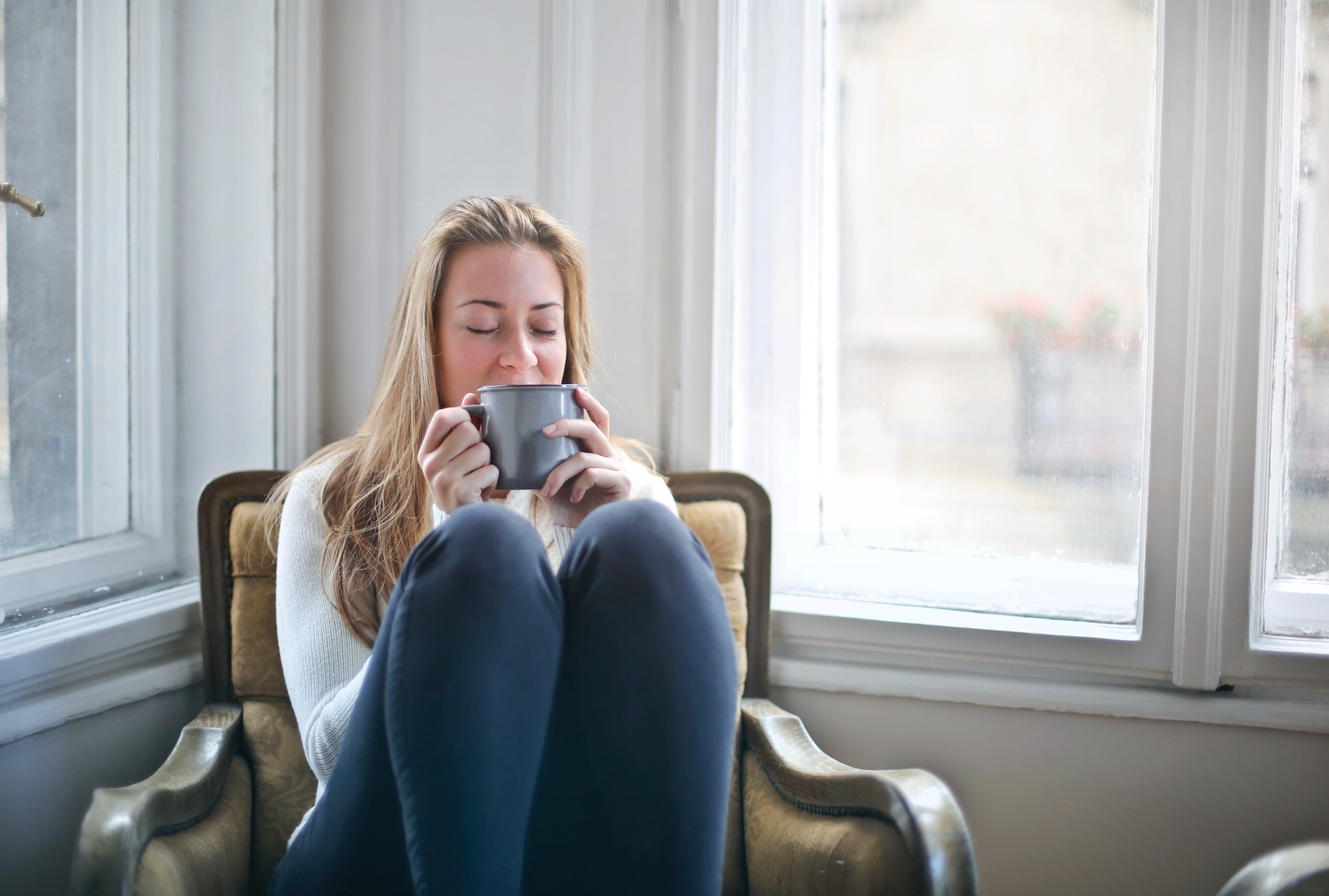 Woman sitting by a window holding a warm mug
